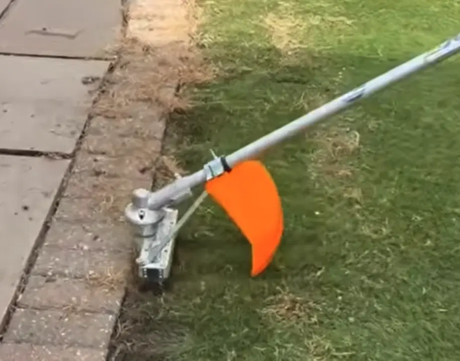 Topkeeper Pro mechanical attachment removing weeds and moss from the edge of an artificial lawn.